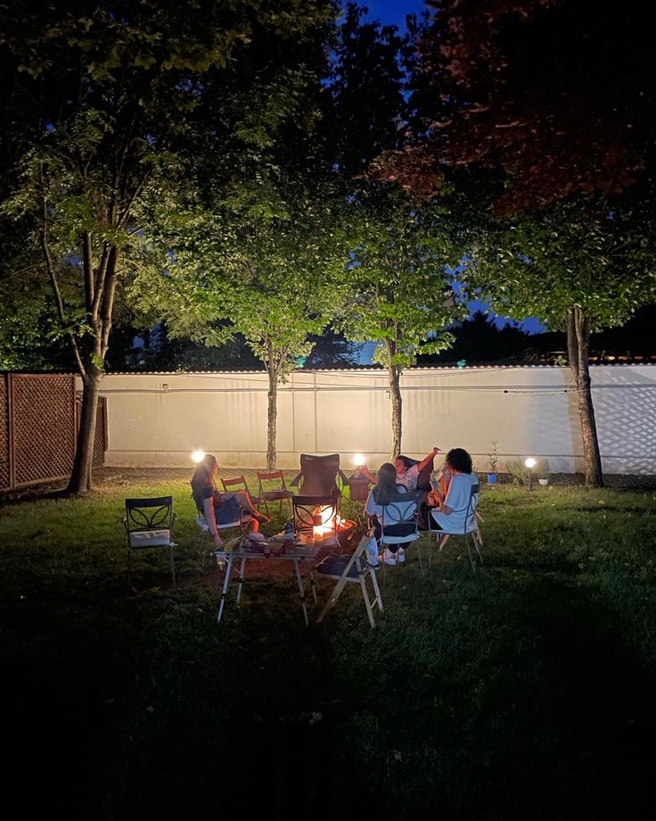 people sitting around a fire pit in the backyard at night with their lights turned on