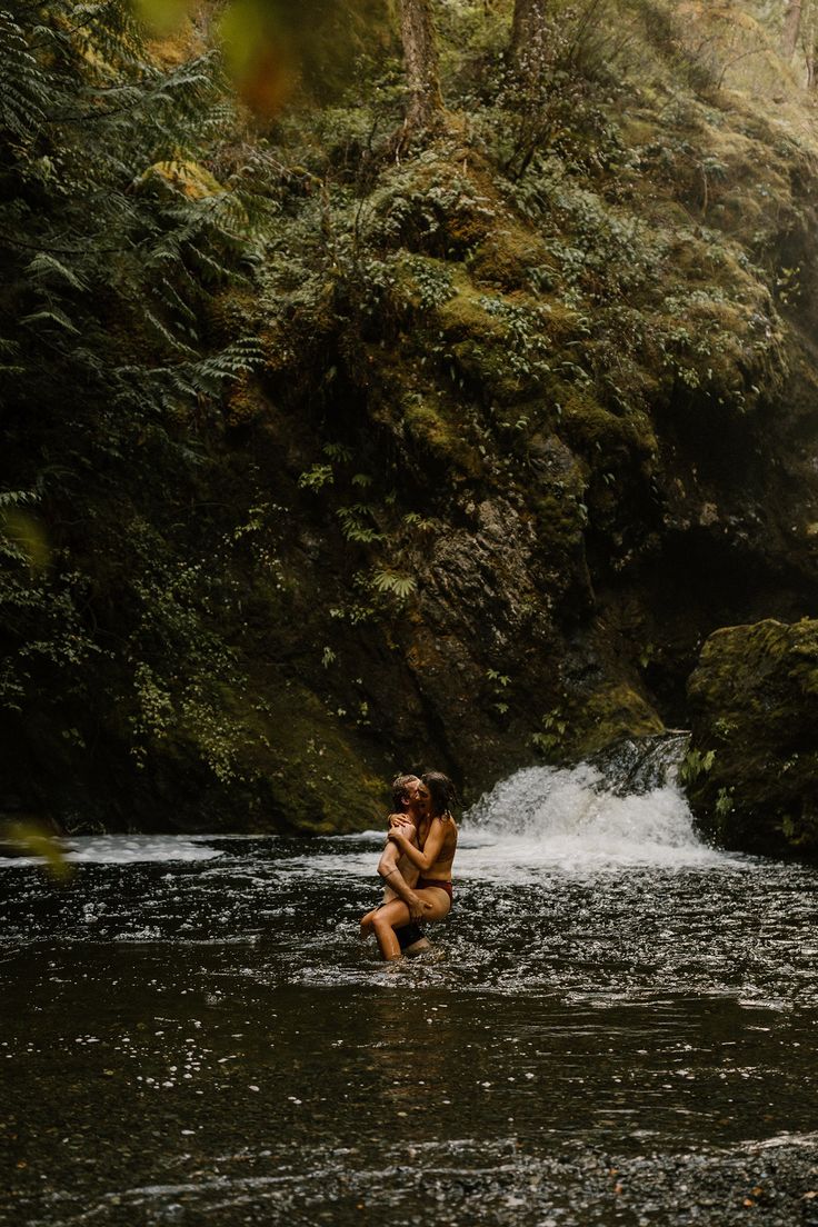 a naked woman wading through a river in the woods