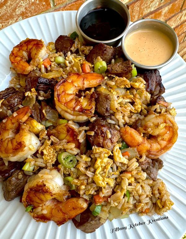 a white plate topped with rice and shrimp next to dipping sauce on a wooden table