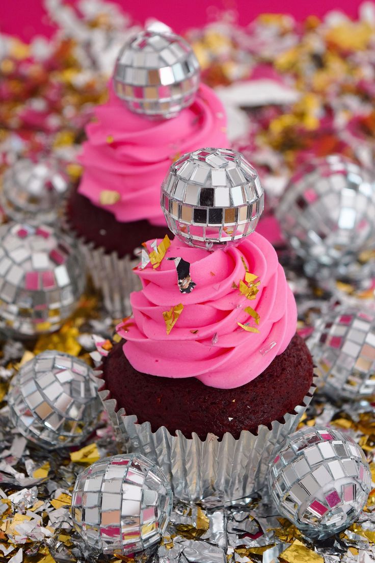 three cupcakes with pink frosting and disco balls on the top are surrounded by confetti