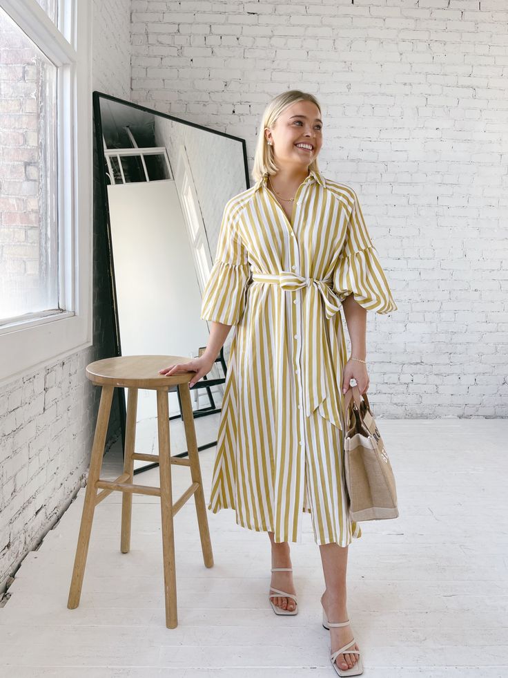 The Ischia Stripe Dress is a shirt dress with flair. Featuring a button down front, shirt collar, tie belt and drop shoulder to an oversized bubble sleeve and pockets. Pair with white tennis shoes or a pair of nude sandals to complete a perfect summer look. Fit: True to sizeFabric Content: 80% Rayon 20% NylonFabric Care: Machine Wash Cold Gentle Cycle, lay flat to dryMeasurements: 45" Shoulder to hemLining: NoZipper: No S:0-2 M:4-6 L:8-10 Yellow Striped Dress, Tee Bag, White Tennis Shoes, Nude Sandals, York Dress, Bubble Sleeve, Mother Denim, Stripe Dress, Summer Look