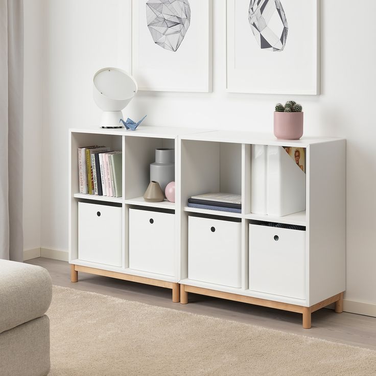 a white bookcase with four bins and two pictures on the wall behind it