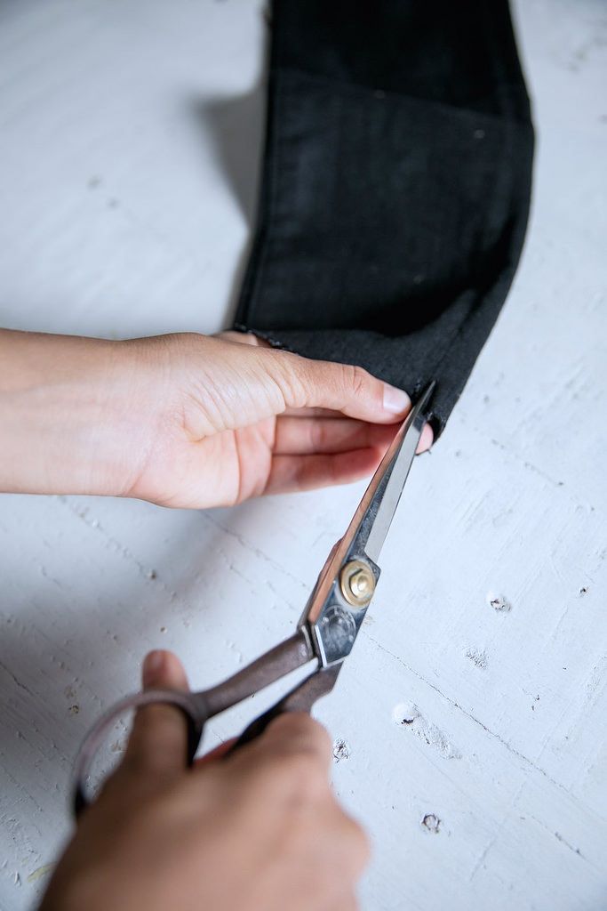 someone is cutting fabric with scissors on a white counter top in front of a pair of black pants