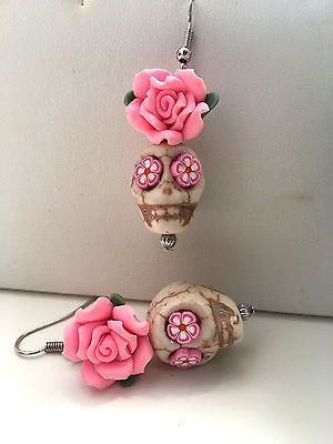 two earrings with pink roses on them sitting next to each other in front of a white wall