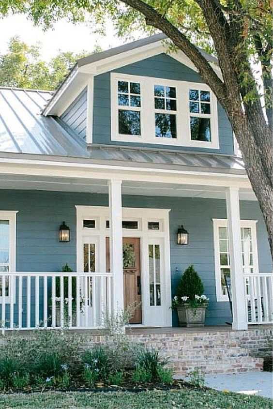 a blue house with white trim on the front porch and two story windows that are open to let in light