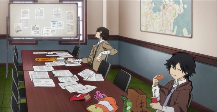 two people sitting at a long table with papers on it in front of a map