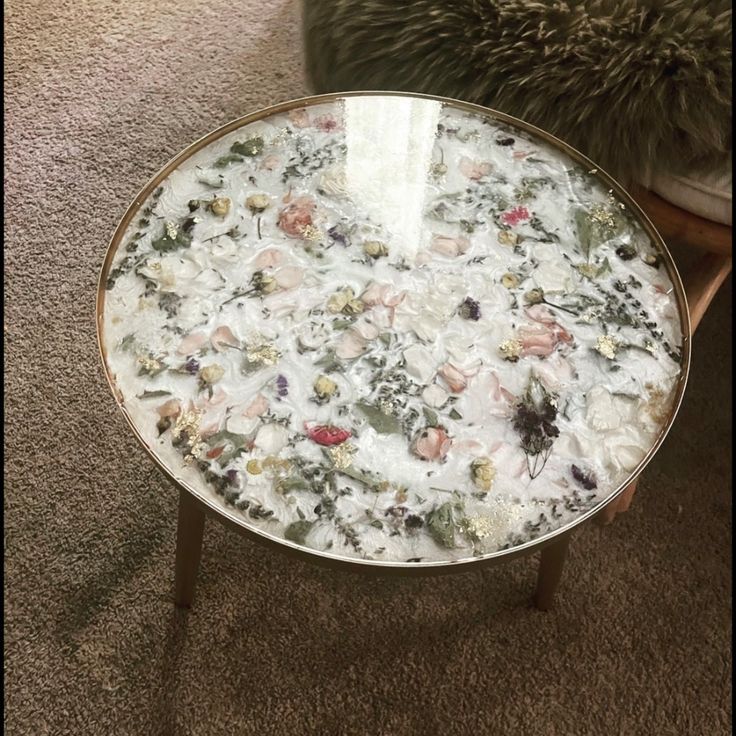 a glass table with flowers on it in the middle of a carpeted room next to a pillow