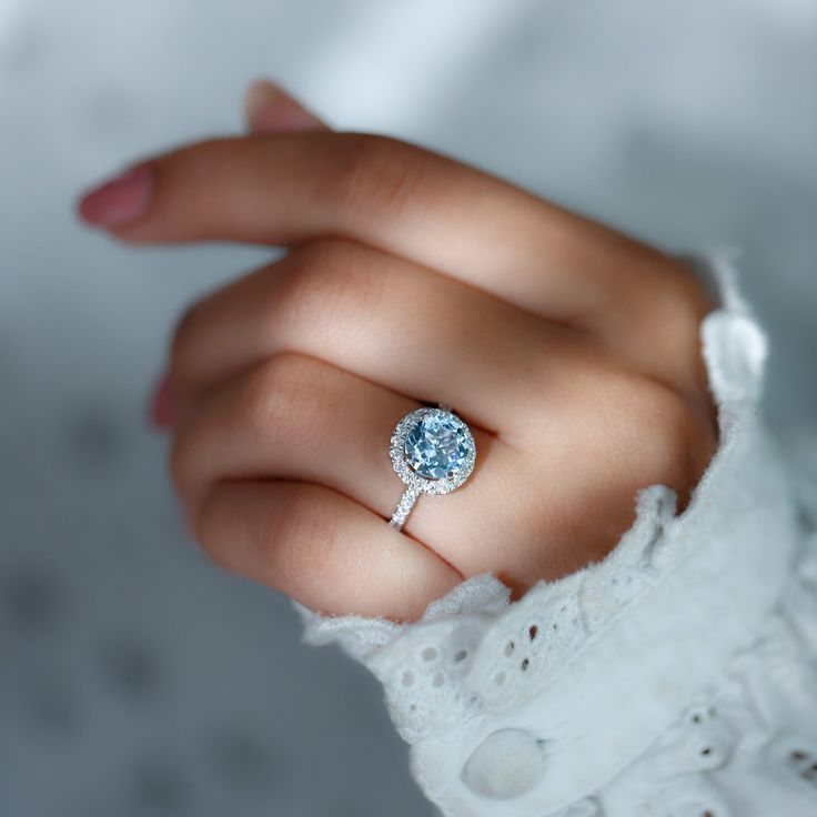 a close up of a person's hand holding a ring with a blue diamond