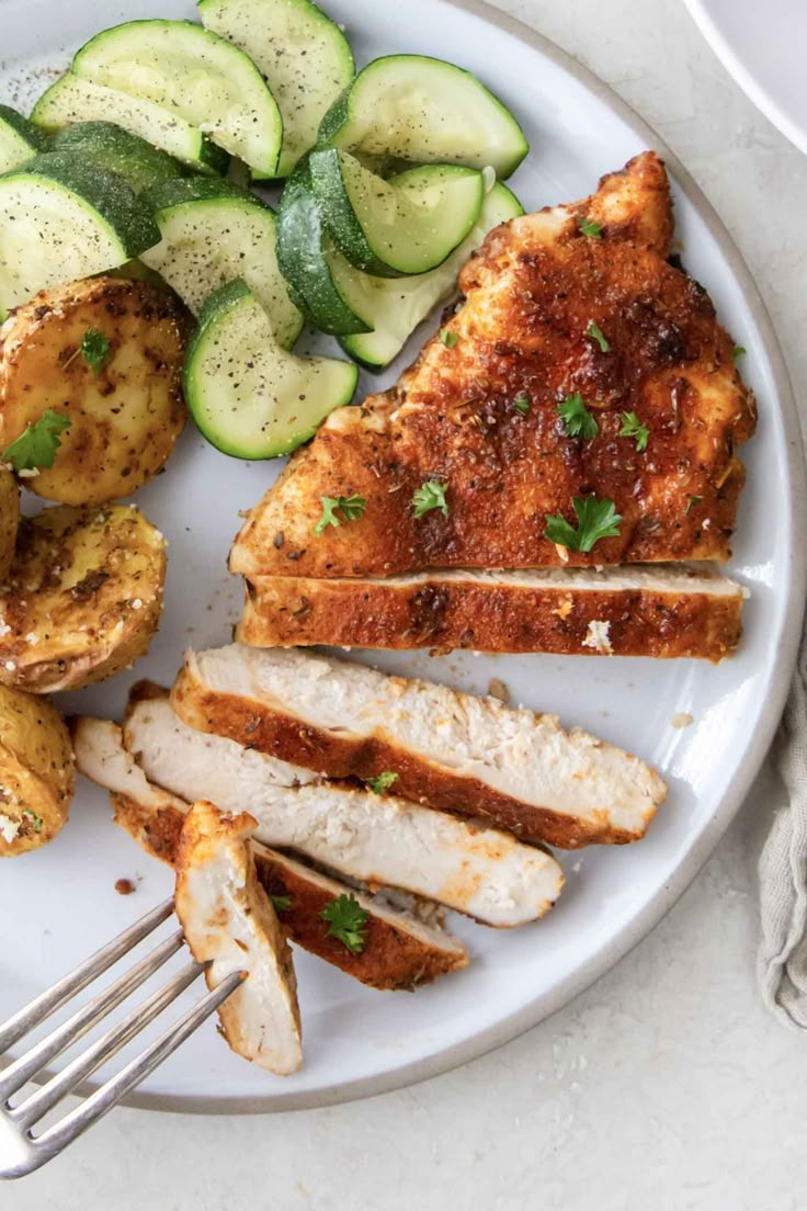 a white plate topped with chicken, potatoes and cucumbers next to a fork