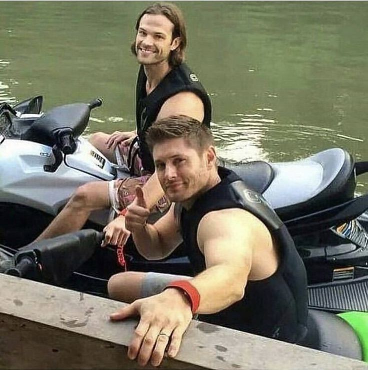 two people on a motorbike in the water next to a wooden rail and boat