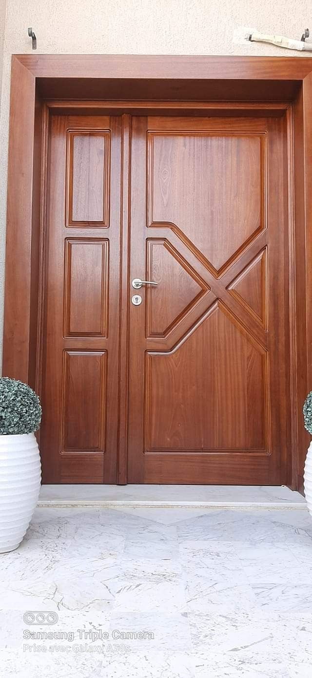 two white vases with flowers are sitting in front of a wooden door that is on the side of a building