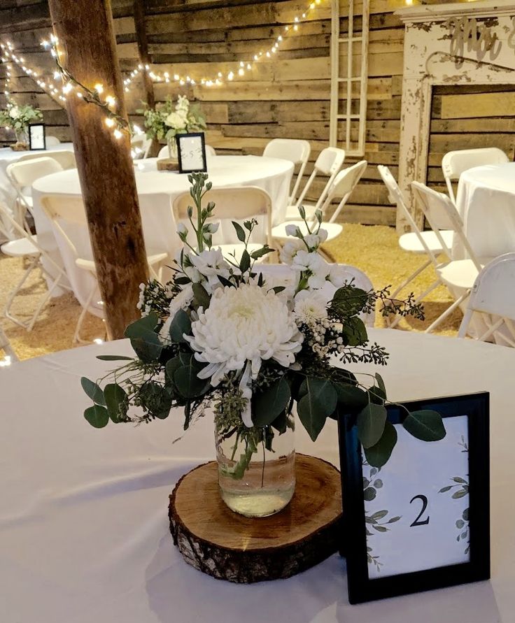 a vase filled with white flowers sitting on top of a wooden table next to a sign