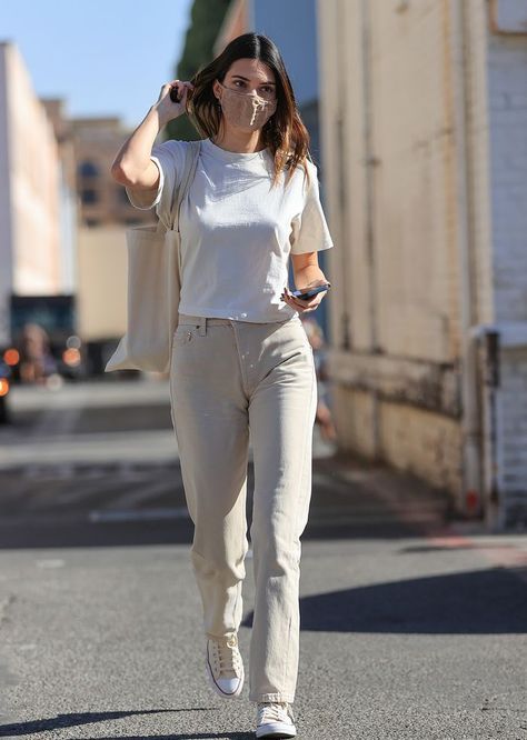 a woman is walking down the street with her cell phone in her hand and she's wearing beige pants