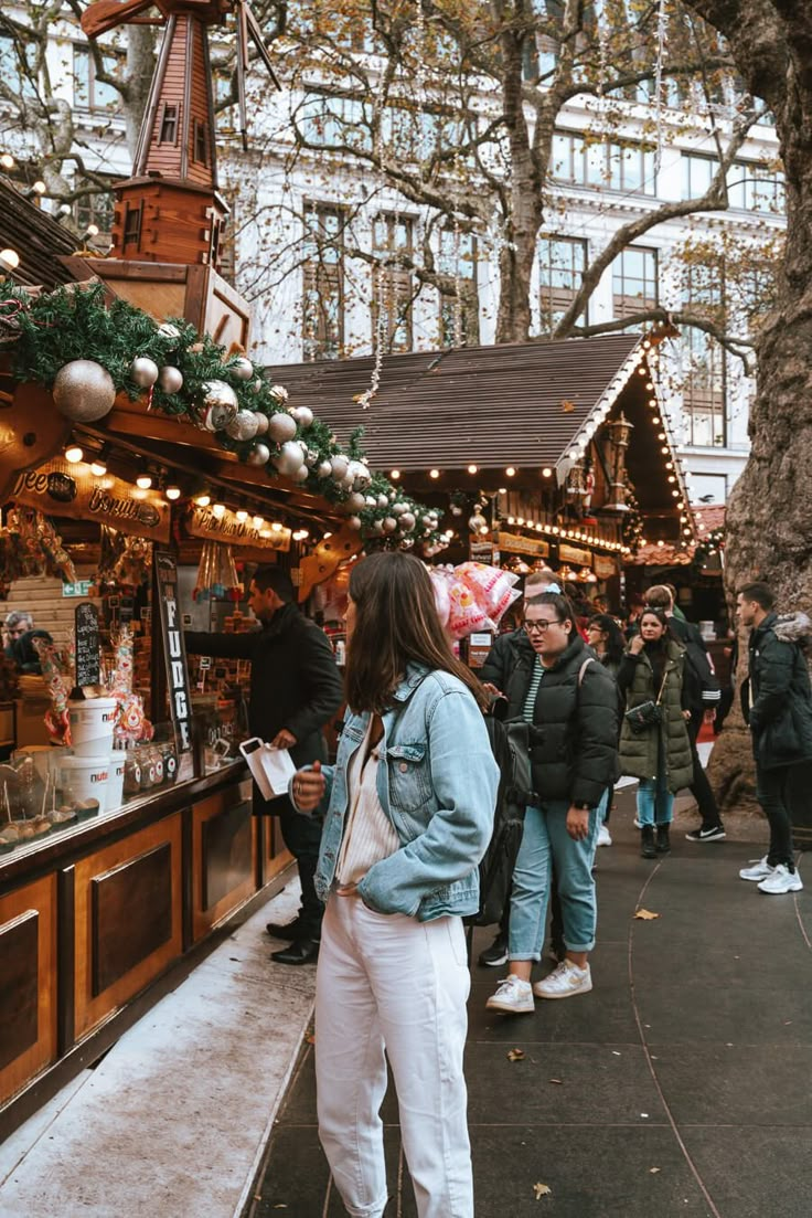 a woman standing in front of a christmas market with lots of people looking at items