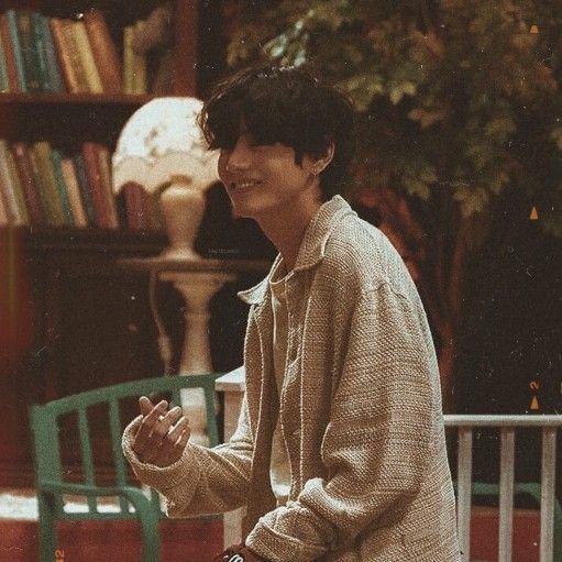 a young man sitting on a bench in front of a bookshelf