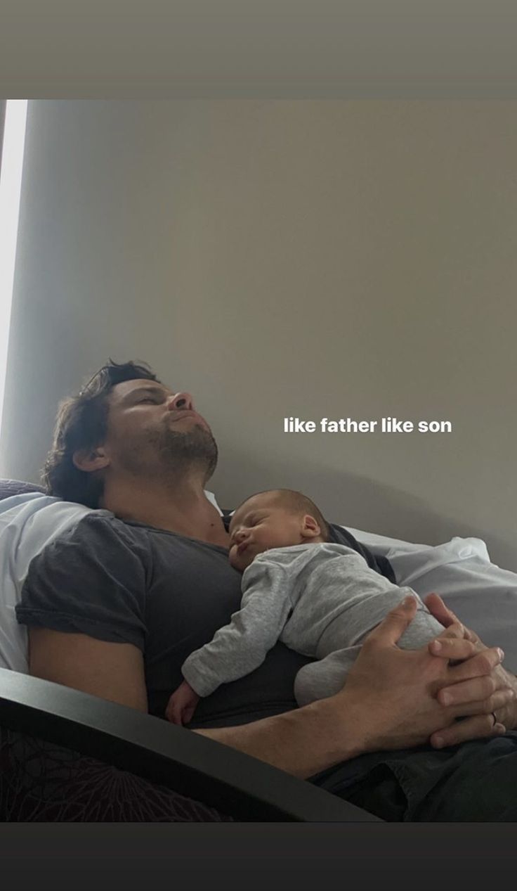 a man laying in bed holding a baby and looking up at the sky with his eyes closed