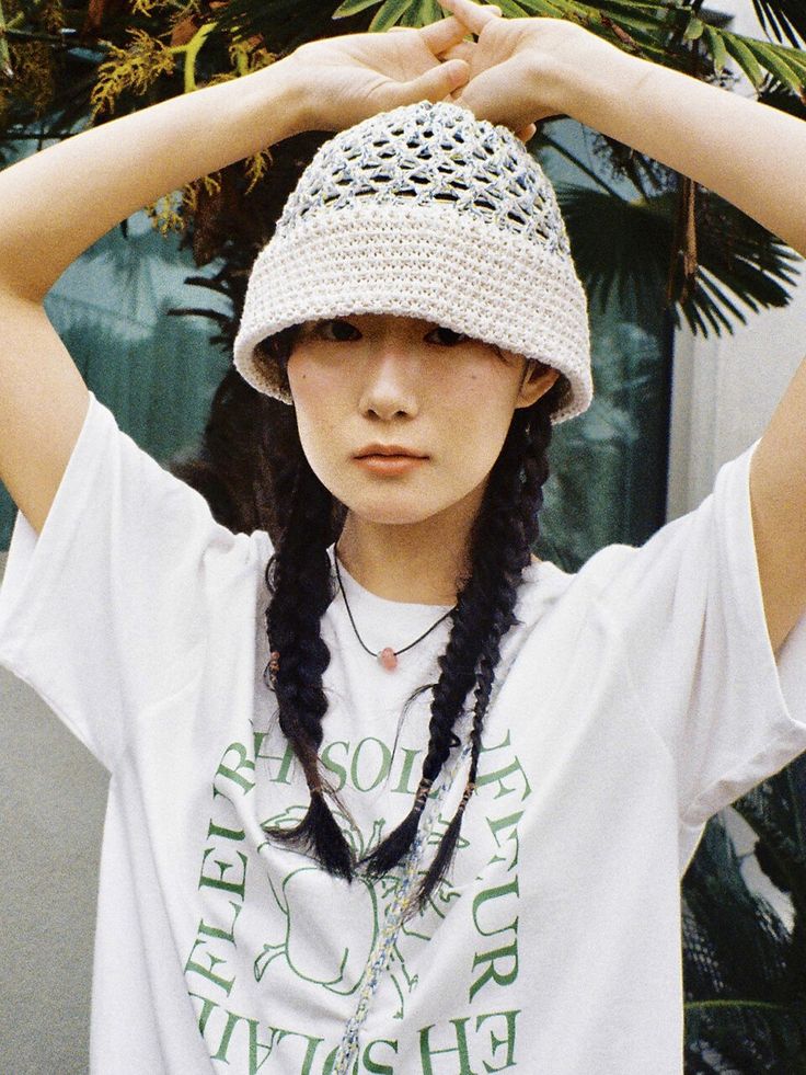 a young woman wearing a crochet hat and braids standing in front of a palm tree