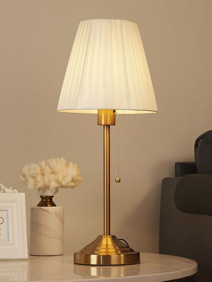 a table with a lamp on top of it next to a white vase filled with flowers