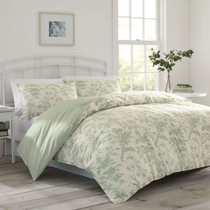 a white bed with green comforter and pillows in a room next to a window