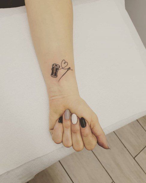 a woman's hand with a small tattoo on her left wrist and a sewing needle in the middle