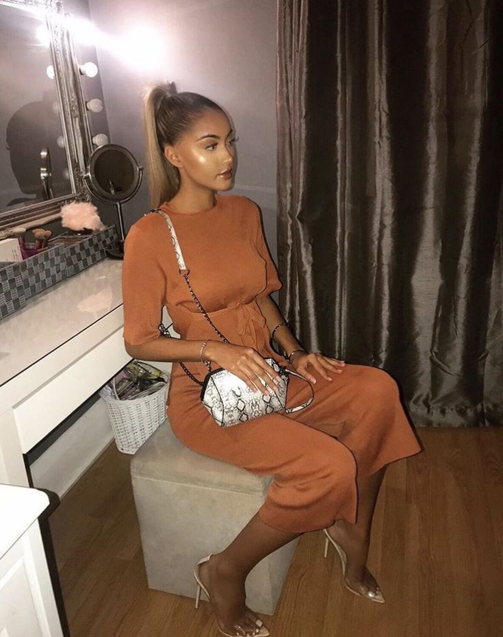 a woman sitting on a stool in front of a mirror holding a purse and looking at her reflection