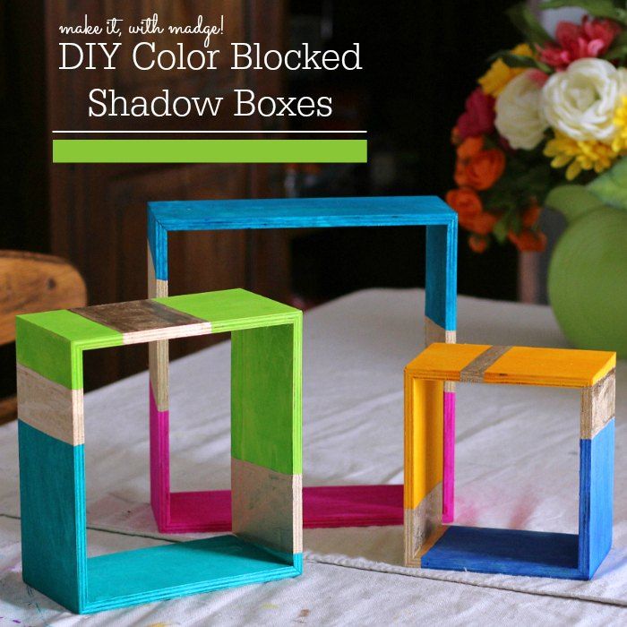 three different colored wooden boxes sitting on top of a white table with flowers in the background