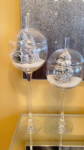 two wine glasses sitting on top of a glass table covered in snowflakes and trees