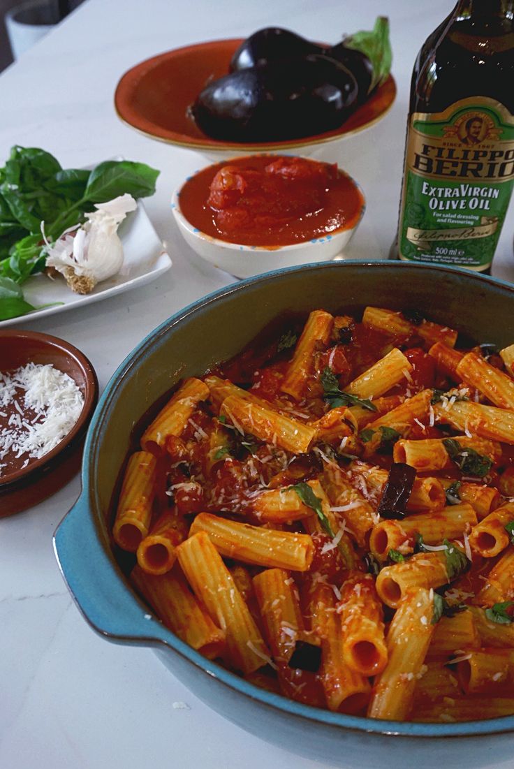 a bowl of pasta and sauce on a table with other food items including basil leaves