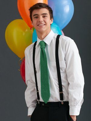 a young man wearing suspenders and a green tie standing in front of colorful balloons