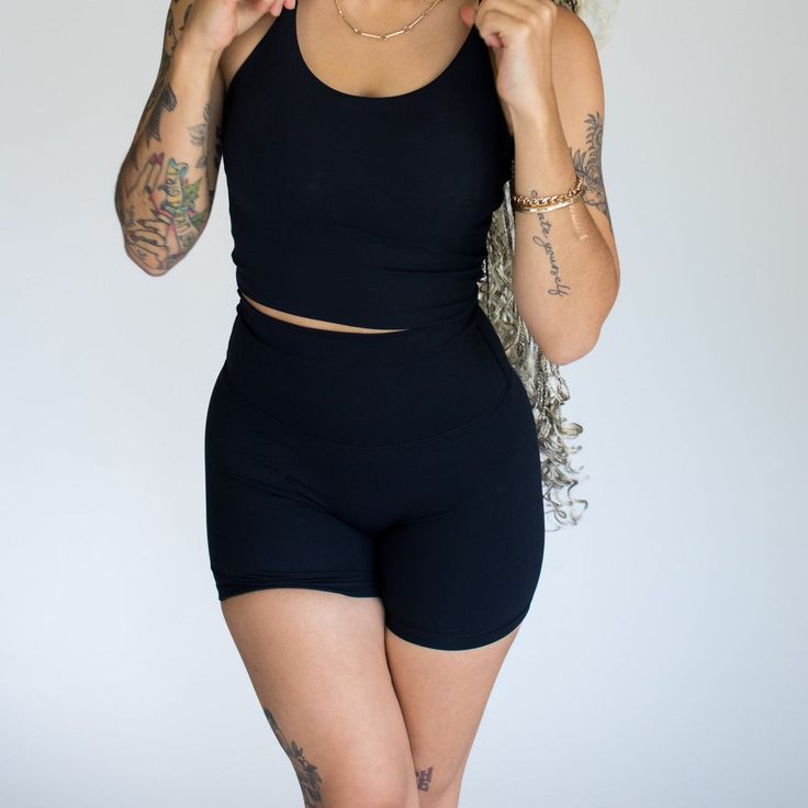 a woman in black shorts and tank top posing for the camera with tattoos on her arms