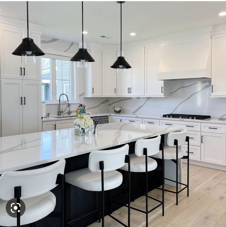 a large kitchen with white cabinets and marble counter tops, black bar stools and an island