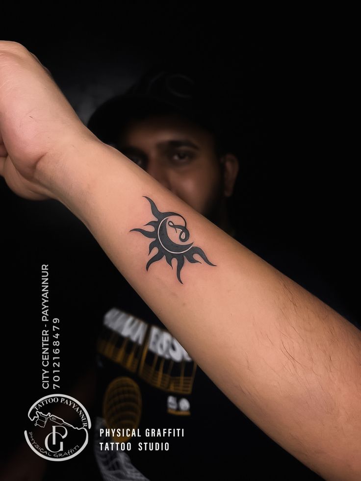 a man with a black tattoo on his arm holding up the sun and moon symbol