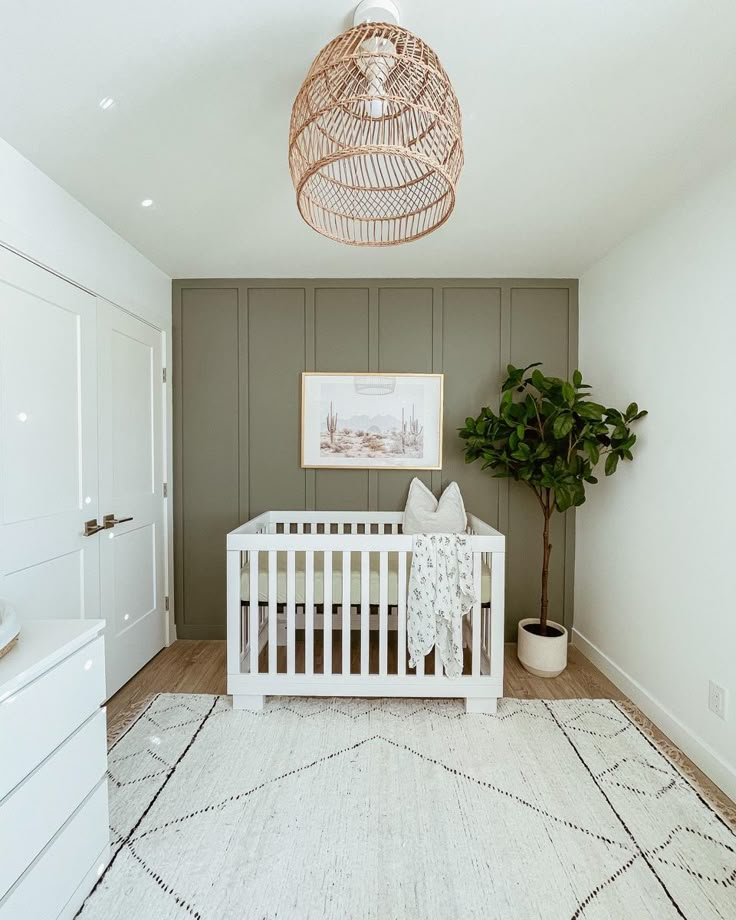 Green feature wall with wicker light fixture and textured rug; plant, white crib, boho art White Crib Green Wall Nursery, Taupe Accent Wall Nursery, Sage Green Nursery With White Crib, White Wicker Nursery, Olive Green And Grey Nursery, Baby Boy Nursery White Crib, Green Feature Wall Nursery, Green White Nursery, Sage Green And White Nursery