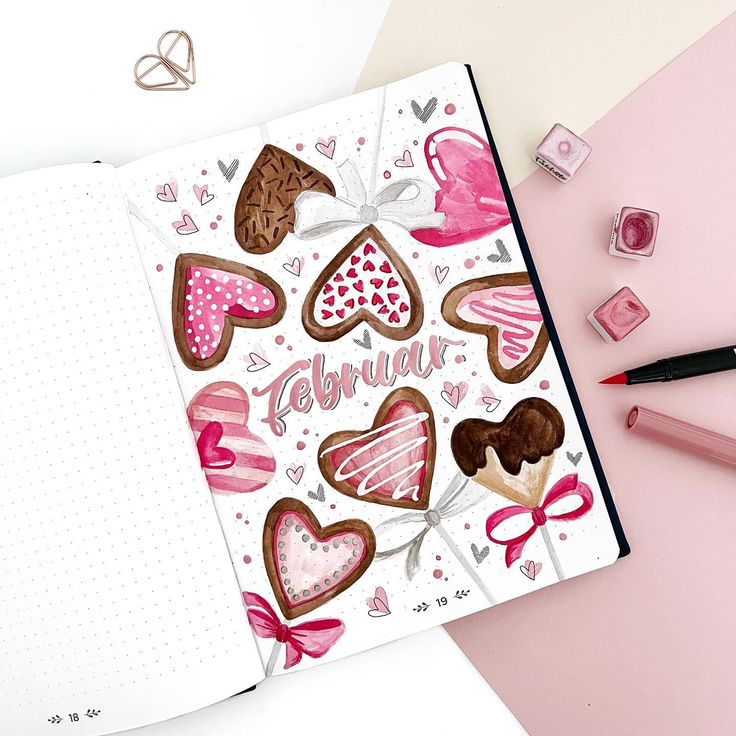 an open notebook with pink and brown hearts on it next to some markers, pencils and marker pens