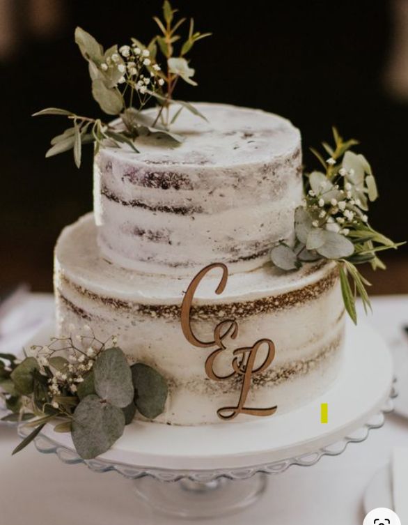 a three tiered wedding cake with greenery and initials on the top is sitting on a table