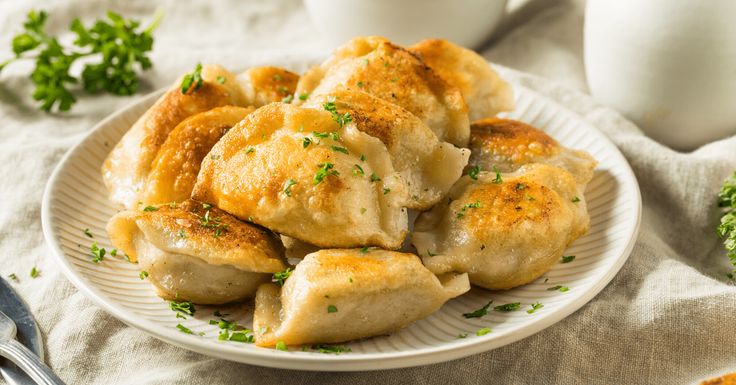 a white plate topped with dumplings and broccoli next to a bowl of sour cream