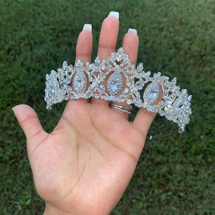 a hand holding two tiaras on top of each other in front of some grass