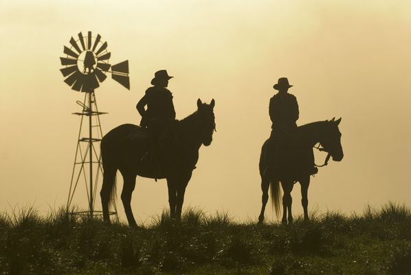 two people riding horses in front of a windmill