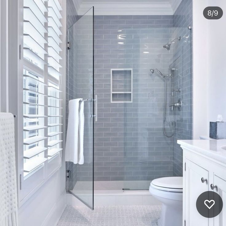 a bathroom with a walk in shower sitting next to a white toilet under a window