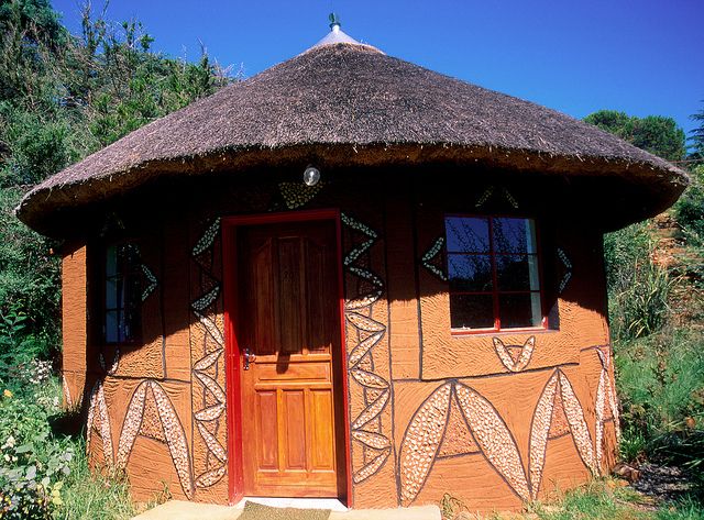 a small hut with a thatched roof and two doors on the outside, surrounded by greenery