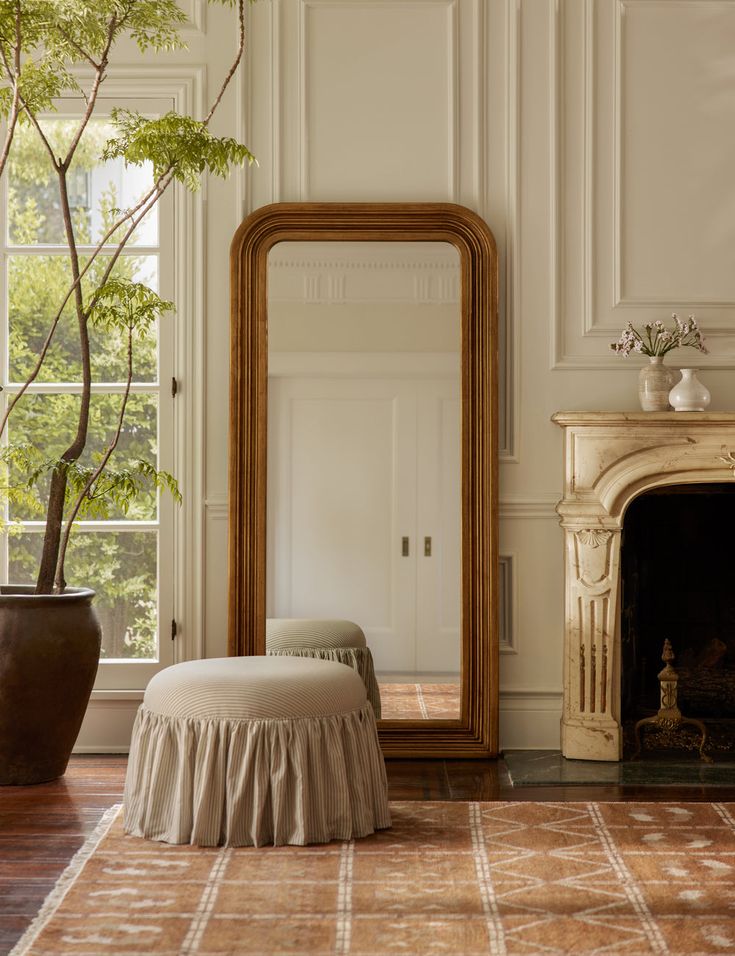 a living room with a fireplace, mirror and ottoman