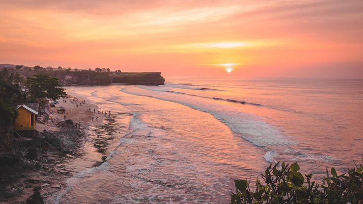 the sun is setting over an ocean with people on the beach and in the water