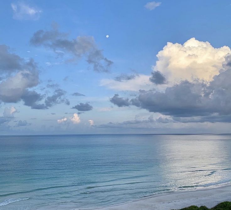 an ocean view with clouds in the sky and some water on the beach near by