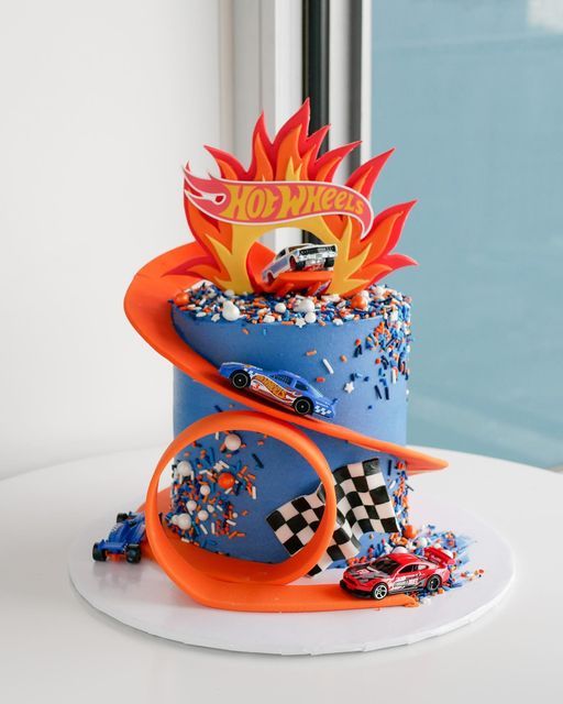 a birthday cake with cars on top and hot wheels decoration around the edges, sitting on a white table