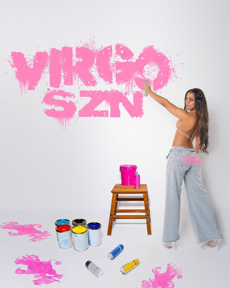 a woman standing in front of a white wall with pink paint on it and the words virgo sin painted all over her body