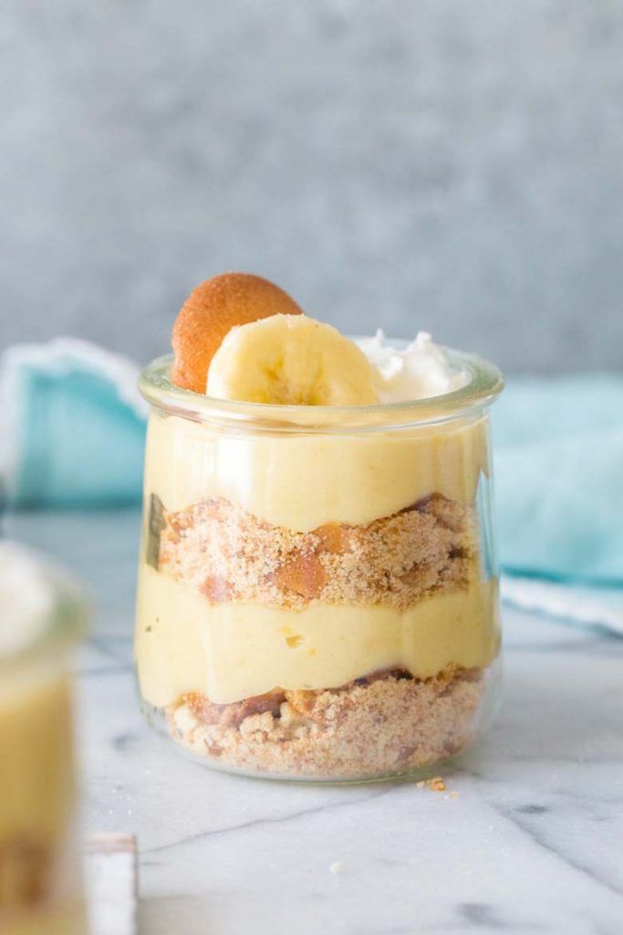 a dessert in a glass jar with bananas and other toppings on the table next to it