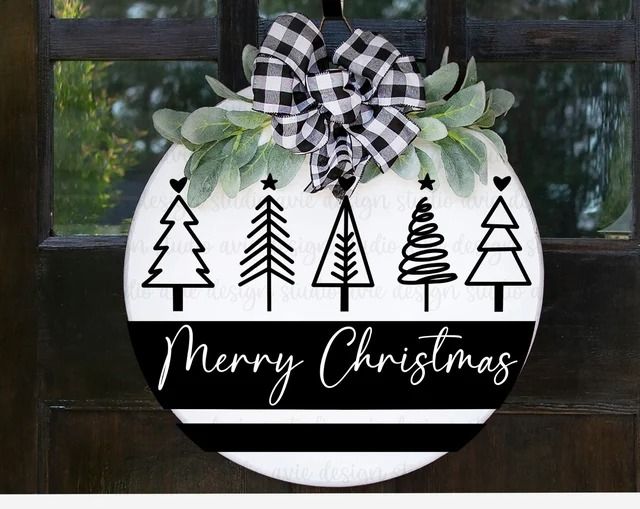 a christmas ornament hanging on a door with evergreens and trees in black and white