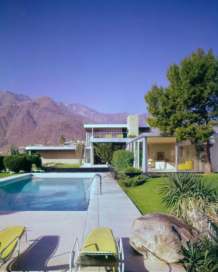 an outdoor swimming pool with lawn chairs and mountains in the background