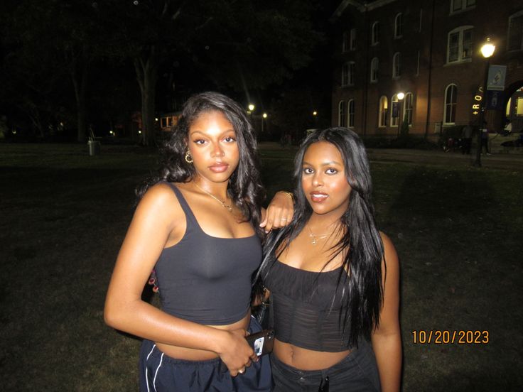 two beautiful young women standing next to each other in front of a building at night