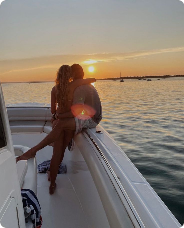 two people sitting on the back of a boat at sunset